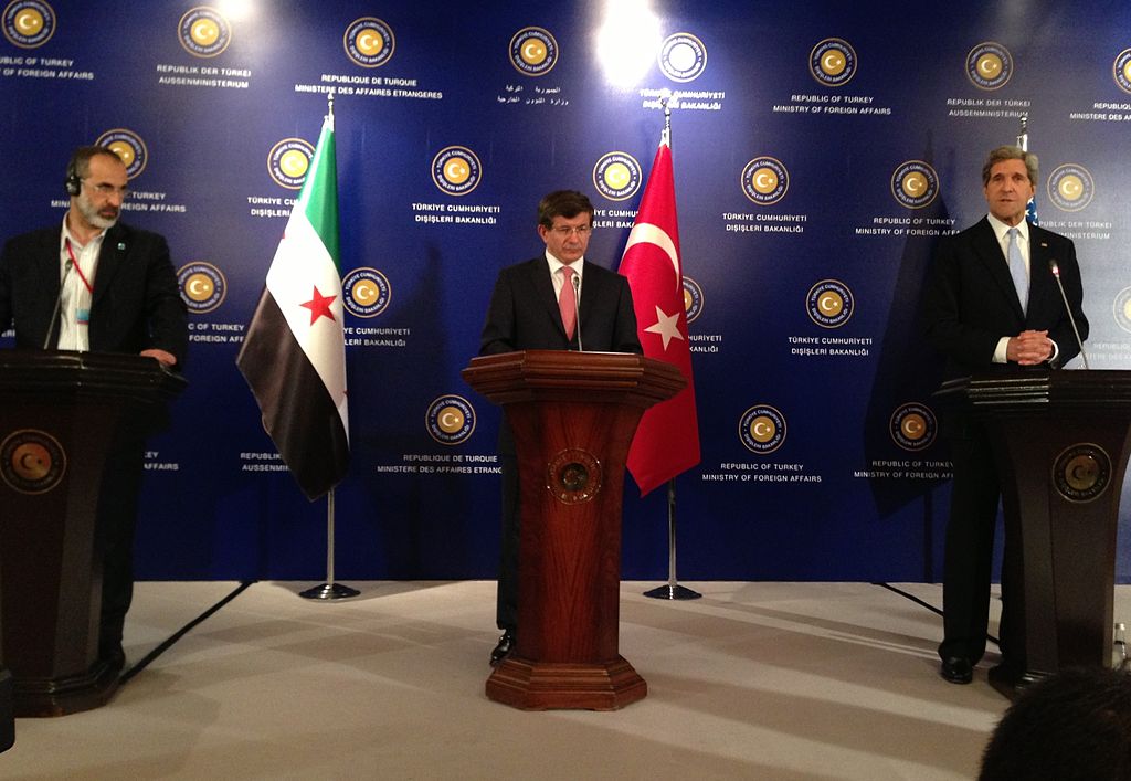 Davutoğlu with John Kerry and Syrian Opposition Council Chairman Moaz al-Khatib in İstanbul, May 2013 - US Department of via Wikimedia Commons
